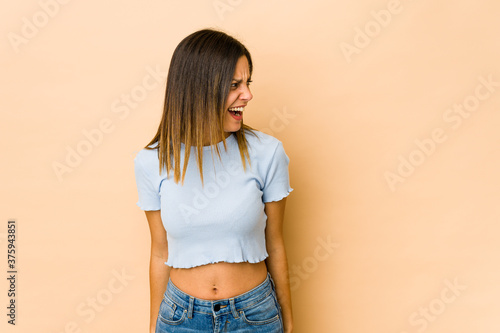 Young woman isolated on beige background shouting very angry, rage concept, frustrated.