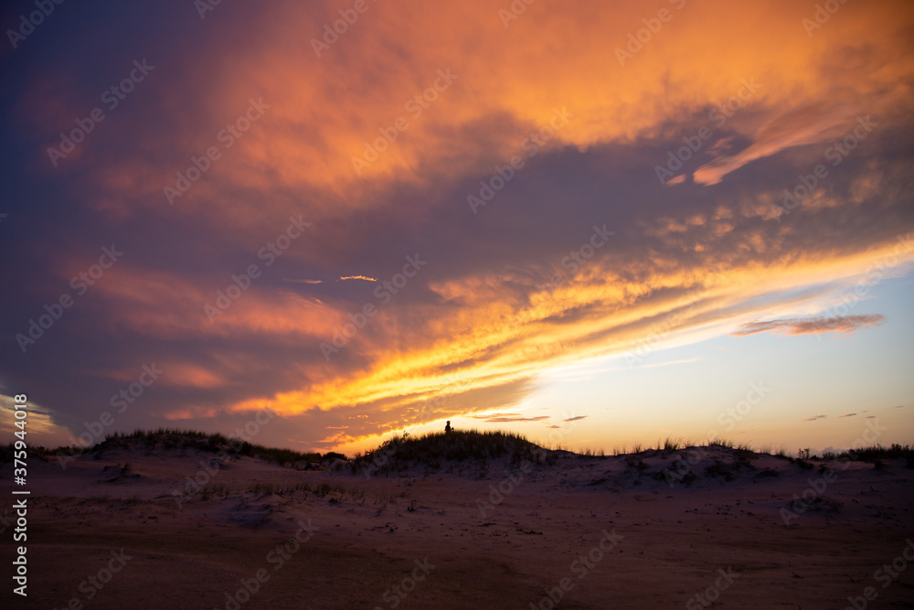 silhouette of photographer on sandy grassy slope at sunset
