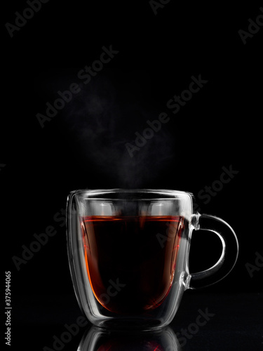 a transparent cup of tea, steam is coming from the tea, the background is dark