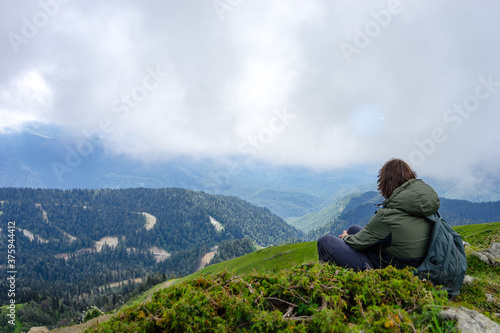 Fototapeta Naklejka Na Ścianę i Meble -  Young man sit in beautiful mountains on hiking trip. Active person resting outdoors in  nature. Backpacker camping outside recreation active