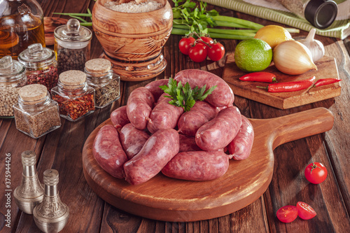 Raw brazilian sausages on the wooden board with ingredients - Linguiça toscana