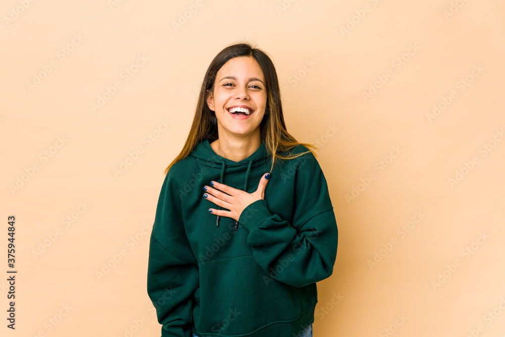 Young woman isolated on beige background laughs out loudly keeping hand on chest. Young woman isolated on beige background laughs out loudly keeping hand on chest.
