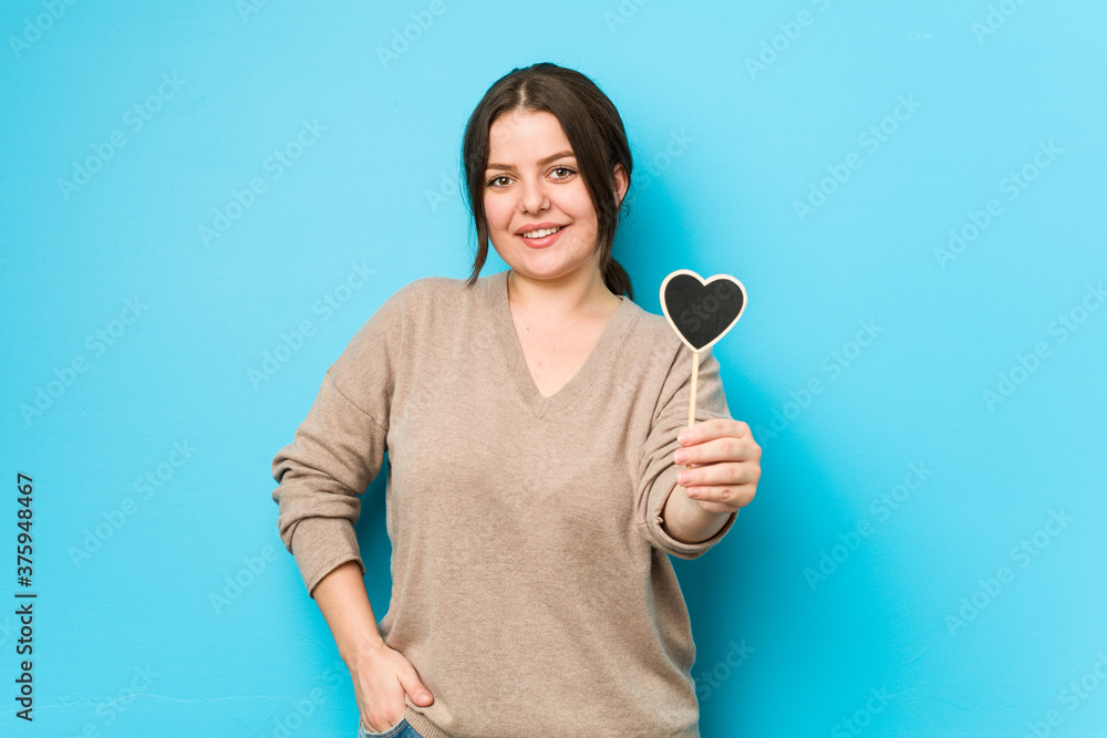 Young plus size curvy woman holding a heart shape happy, smiling and cheerful. Young plus size curvy woman holding a heart shape happy, smiling and cheerful.