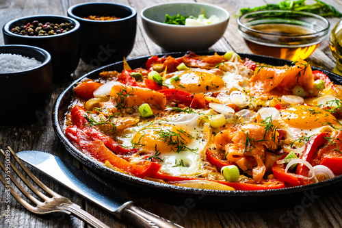 Shakshuka - fried eggs with salmon and vegetables in frying pan 