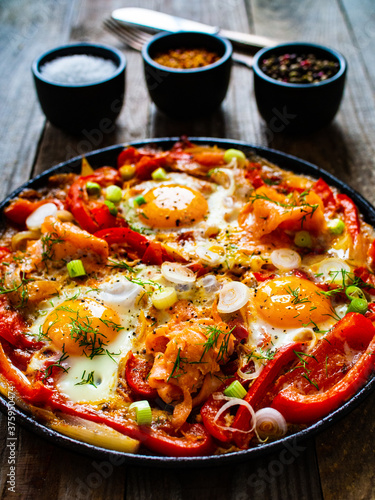 Shakshuka - fried eggs with salmon and vegetables in frying pan
