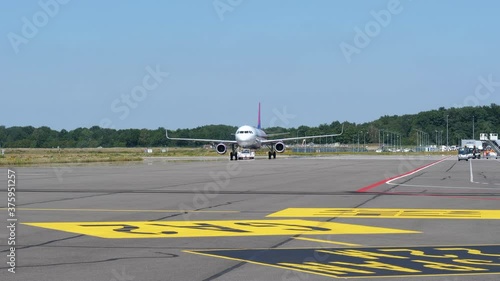 Airplane Parked At The Airport Apron With Baggage Car And Airport Baggage Belt Loader Driving On The Side At Eindhoven Airport In The Netherlands. - wide shot