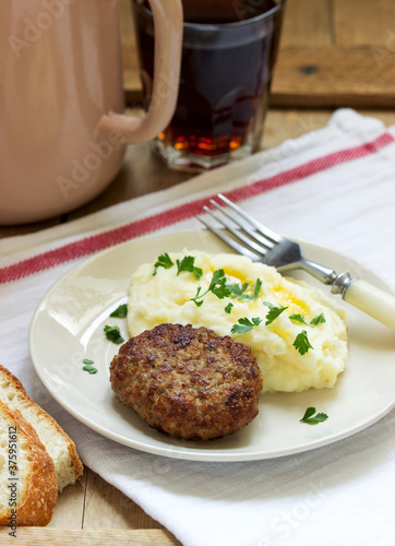 Cutlet, mashed potatoes with butter and parsley and tea on a wooden table.