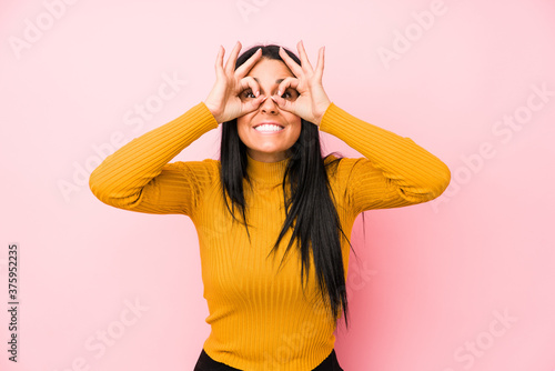 Young caucasian woman isolated on a pink background showing okay sign over eyes