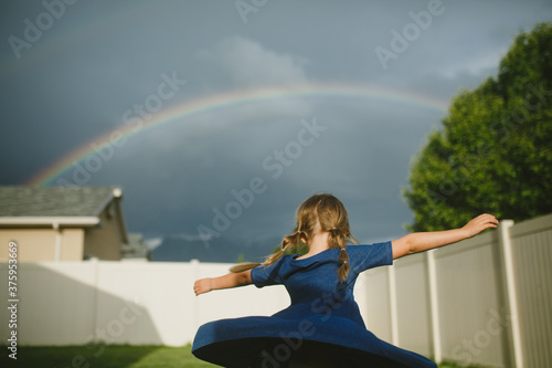 Little girl spinning in her backyard with a rainbow overhead