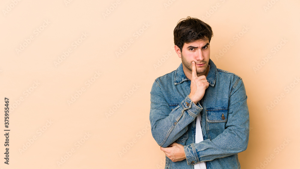 Young man isolated on beige background looking sideways with doubtful and skeptical expression. Young man isolated on beige background looking sideways with doubtful and skeptical expression.