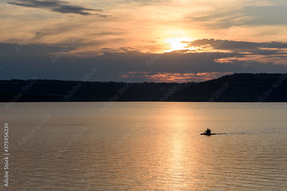 Beautiful sunset over a large lake among the hills. The couple floats on a catamaran on the lake and admire the sunset. Lake Bakota and the Dniester River. Summer tourist destinations in Ukraine