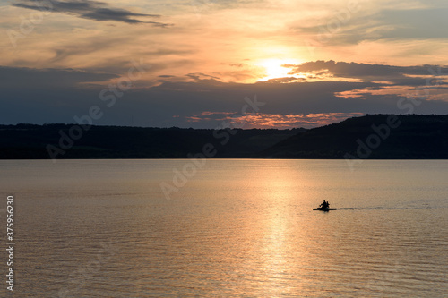 Beautiful sunset over a large lake among the hills. The couple floats on a catamaran on the lake and admire the sunset. Lake Bakota and the Dniester River. Summer tourist destinations in Ukraine