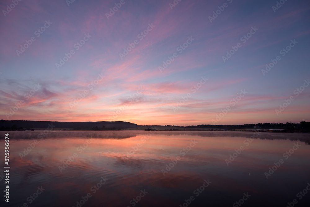 Pink sky over the lake with haze above the water in the morning before dawn