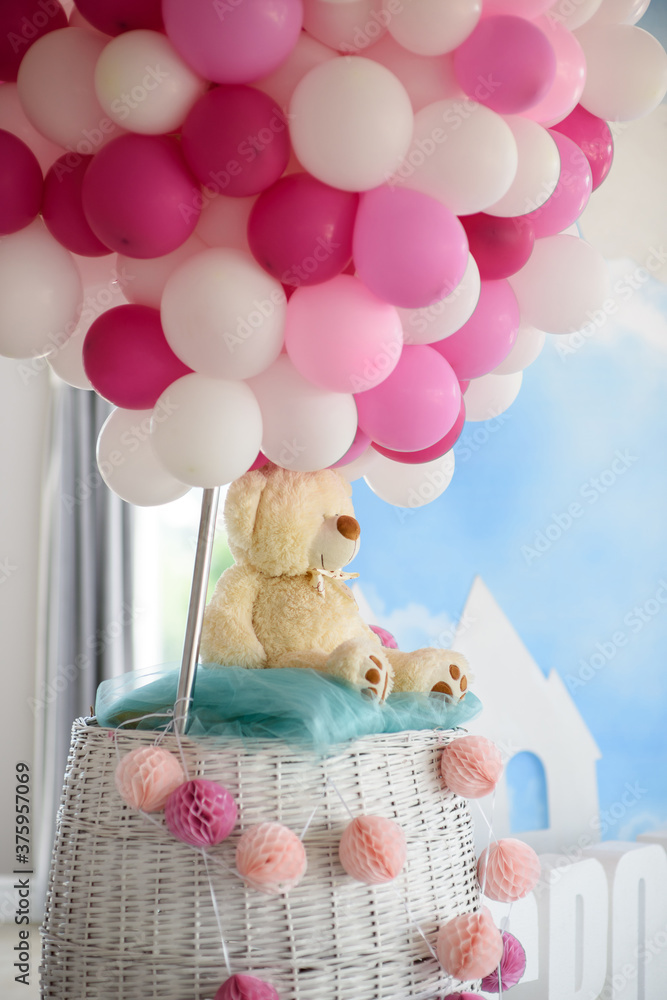 Stylish and modern decoration for a children's party with a toy teddy bear in a basket and white, pink and raspberry balloons Stylish and modern decoration for a children's party with a toy teddy bear in a basket and white, pink and raspberry balloons