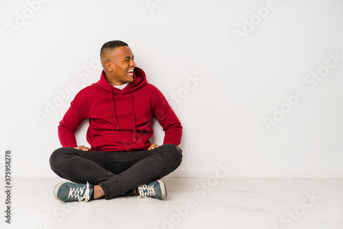 Young latin man sitting on the floor isolated shouting towards a copy space