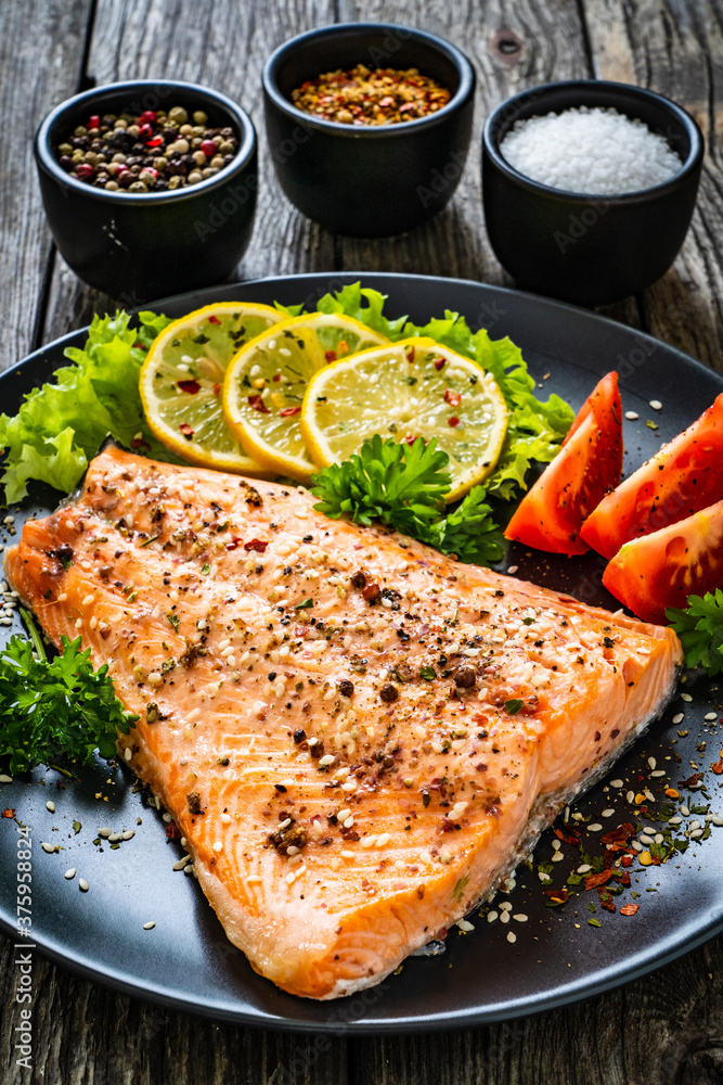 Fried salmon fillet with lettuce, lemon and tomatoes served on black plate on wooden table
Fried salmon fillet with lettuce, lemon and tomatoes served on black plate on wooden table