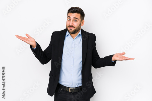 Young caucasian business man against a white background isolated doubting and shrugging shoulders in questioning gesture. photo