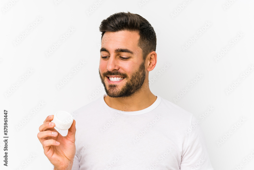 Young caucasian man holding a moisturizer isolated smiling confident with crossed arms. Young caucasian man holding a moisturizer isolated smiling confident with crossed arms.