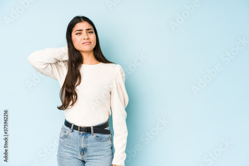 Young indian woman isolated on blue background touching back of head, thinking and making a choice.