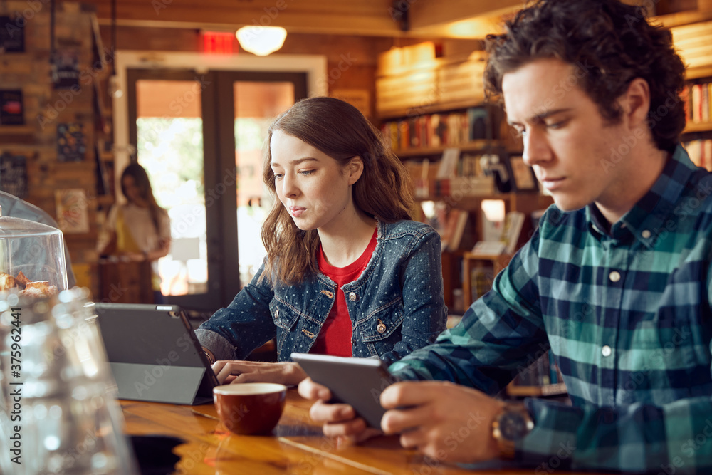 Young man and woman sitting at counter in cafe bookstore using digital tablets Young man and woman sitting at counter in cafe bookstore using digital tablets