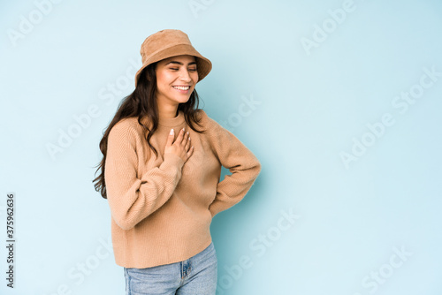 Young indian woman wearing a hat isolated on blue background laughing keeping hands on heart, concept of happiness.