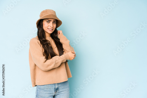 Young indian woman wearing a hat isolated on blue background massaging elbow, suffering after a bad movement.