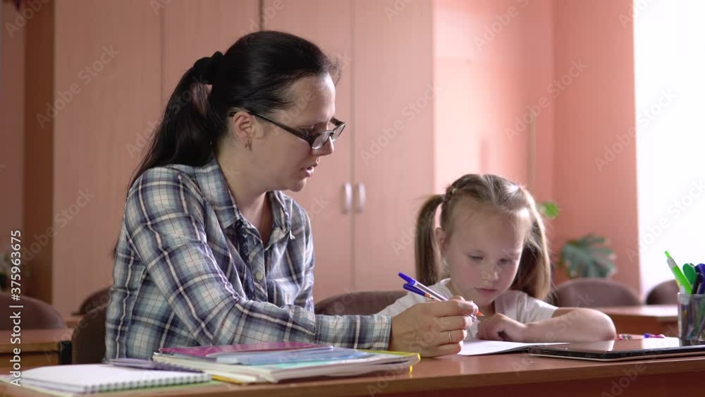 Little beautiful girl is studies with the teacher in the school class. Draws in a notebook with a pen. Preschool education.4k Little beautiful girl is studies with the teacher in the school class. Draws in a notebook with a pen. Preschool education.4k