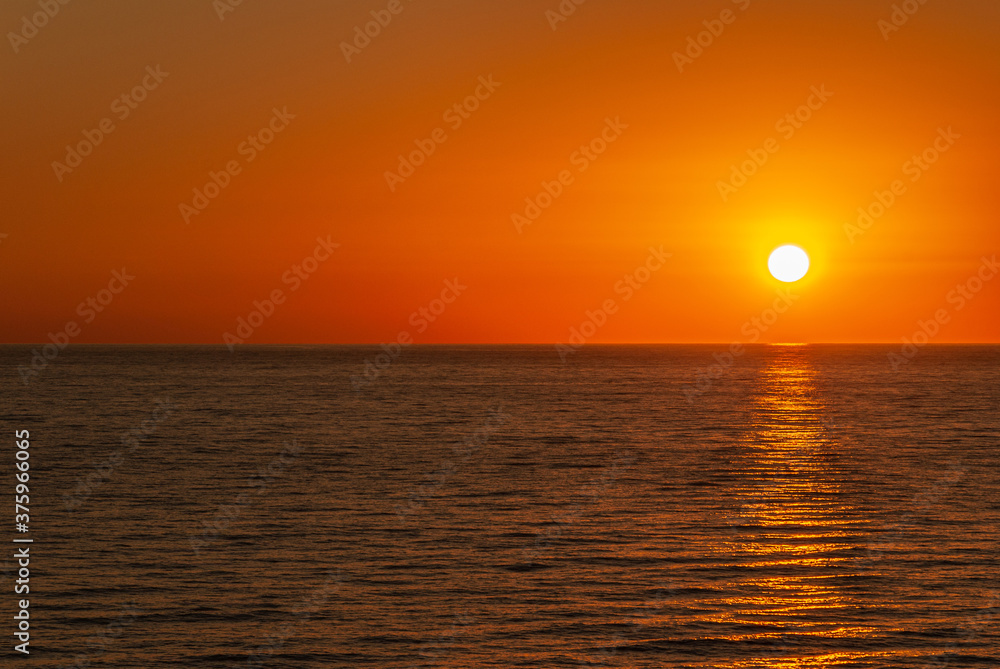 Cabo San Lucas, Mexico - November 23, 2008: Red sky sunset above dark Pacific Ocean reflecting orange sun in the evening.