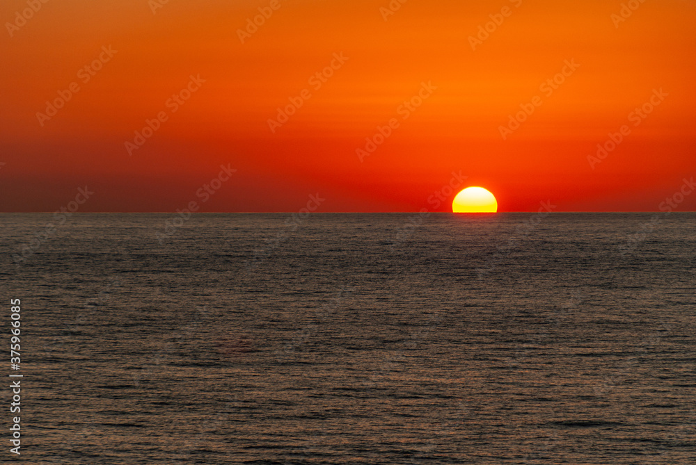 Cabo San Lucas, Mexico - November 23, 2008: Red sky sunset of half-sunk sun into dark Pacific Ocean in the evening.