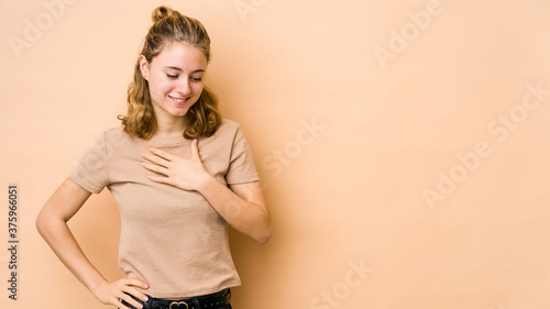 Young caucasian woman isolated on beige background laughing keeping hands on heart, concept of happiness.