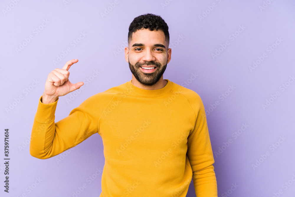 Young mixed race arabic man isolated holding something little with forefingers, smiling and confident. Young mixed race arabic man isolated holding something little with forefingers, smiling and confident.