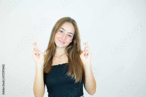 Smiling girl with fingers crossed gesture on white background