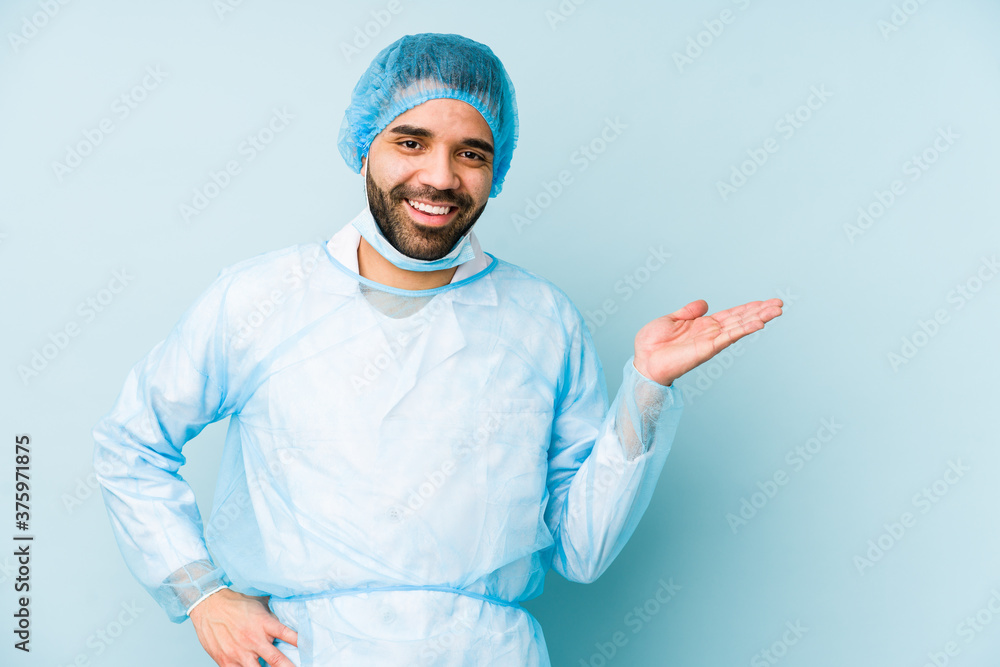 Young surgeon latin man isolated Young dshowing a copy space on a palm and holding another hand on waist.