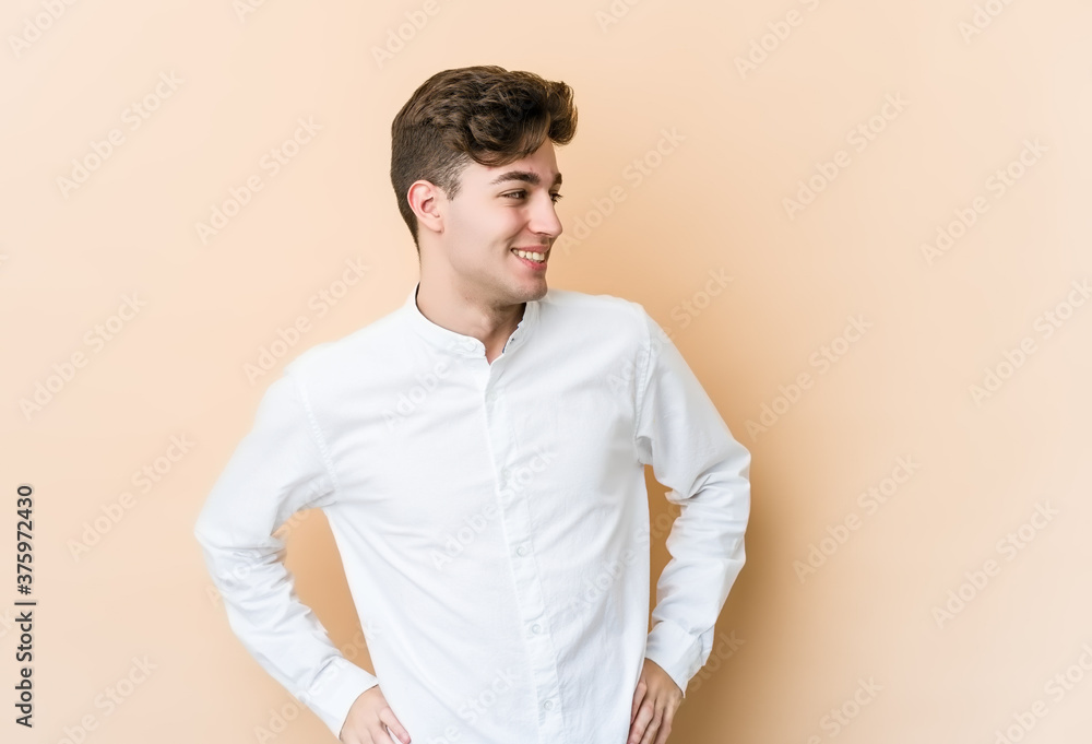 Young caucasian man isolated on beige background laughs happily and has fun keeping hands on stomach. Young caucasian man isolated on beige background laughs happily and has fun keeping hands on stomach.