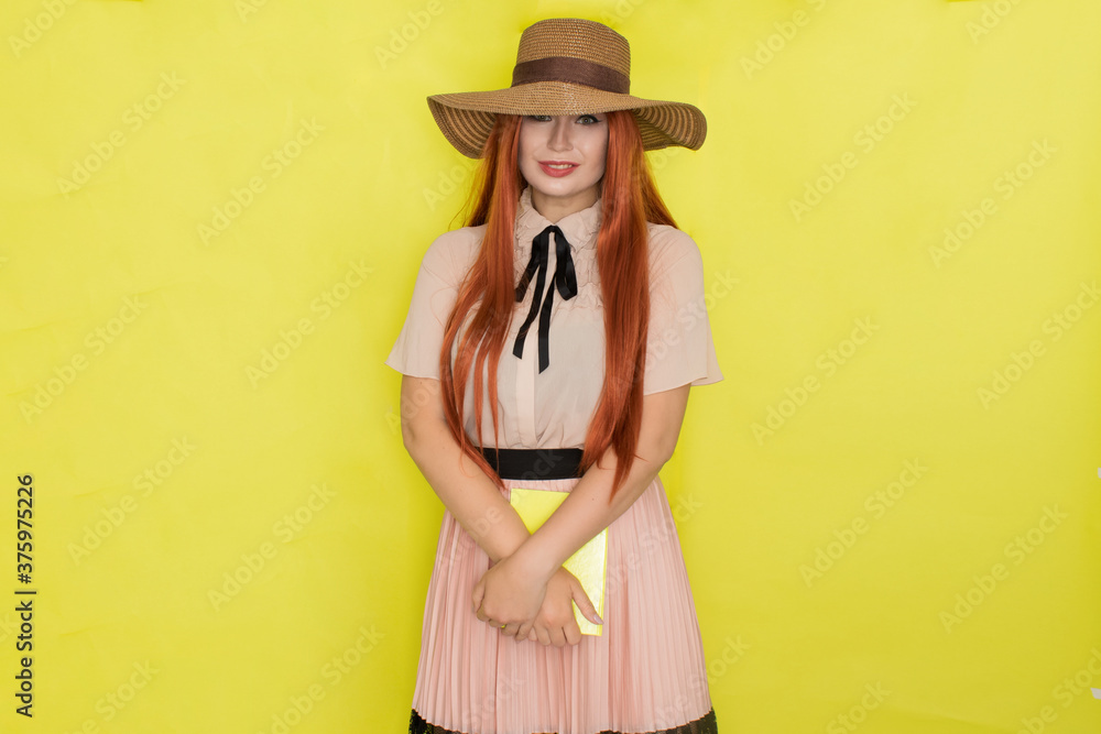 Red haired woman in straw hat over yellow background holding book in her hands Red haired woman in straw hat over yellow background holding book in her hands