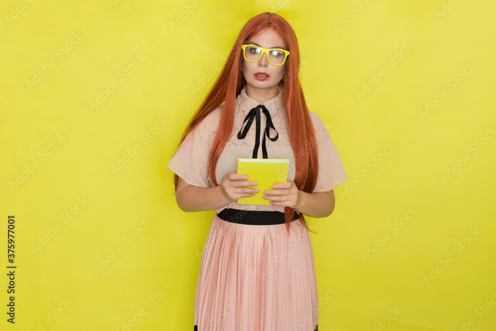 Red haired woman over yellow background holding book in her hands Red haired woman over yellow background holding book in her hands