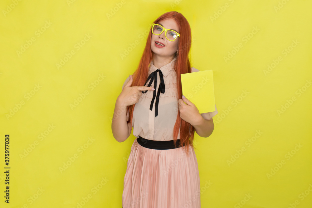 Red haired woman over yellow background holding book in her hands Red haired woman over yellow background holding book in her hands