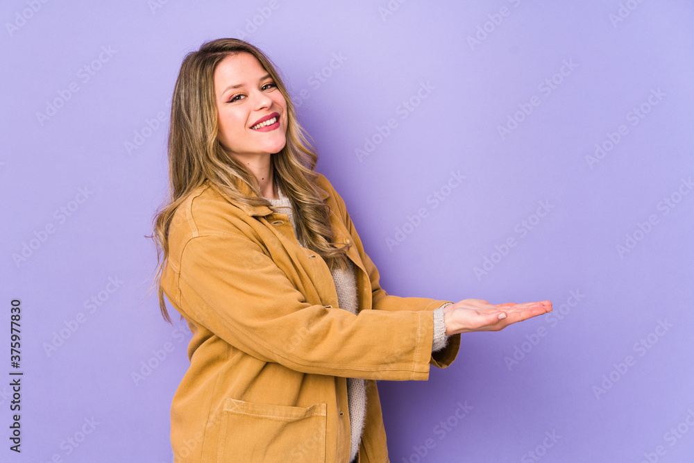 Young caucasian woman isolated on purple background holding a copy space on a palm. Young caucasian woman isolated on purple background holding a copy space on a palm.