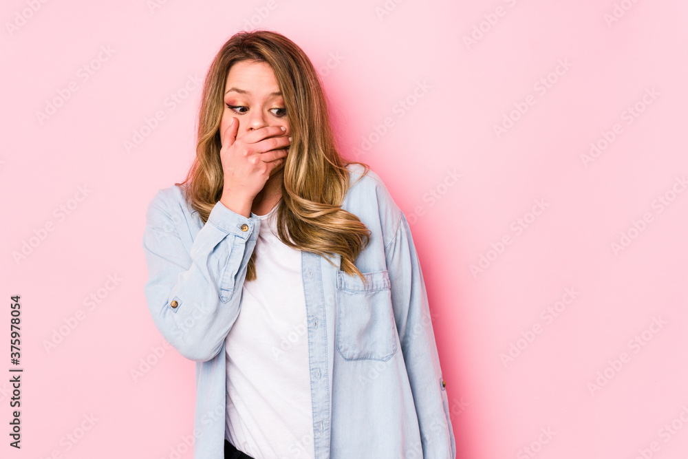 Young caucasian woman isolated on pink background thoughtful looking to a copy space covering mouth with hand.
