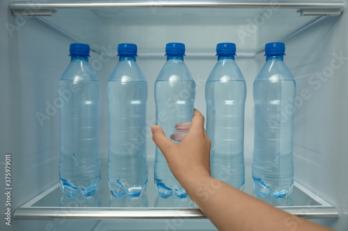 Woman taking bottle of fresh water from fridge shelf, closeup