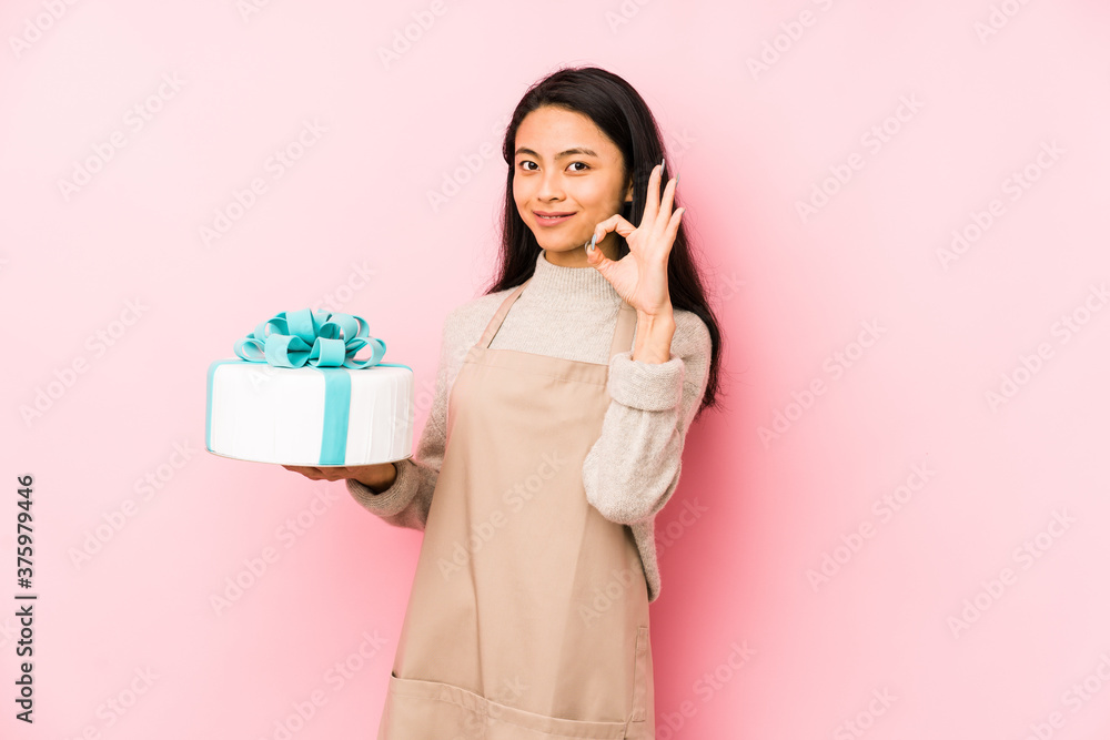 Young chinese woman holding a cake isolated showing fist to camera, aggressive facial expression. Young chinese woman holding a cake isolated showing fist to camera, aggressive facial expression.
