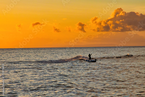 Silhoetted surfer riding a wave at sunset in Lahaina on Maui. © manuel