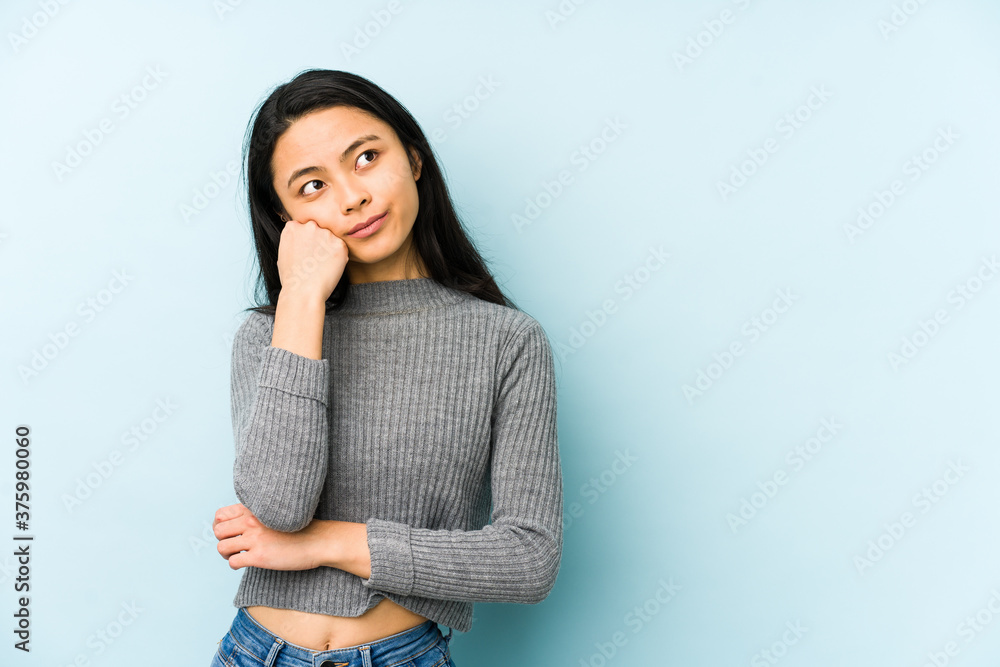 Young chinese woman isolated on a blue background who feels sad and pensive, looking at copy space. - obrazy, fototapety, plakaty 