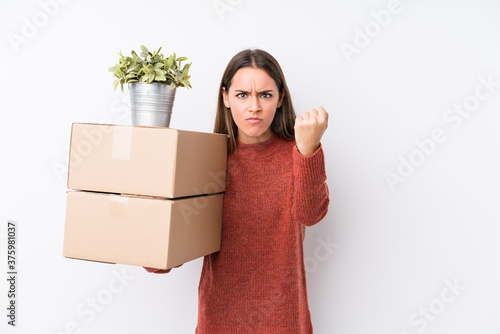 Young caucasic woman holding boxes isolated showing fist to camera, aggressive facial expression.