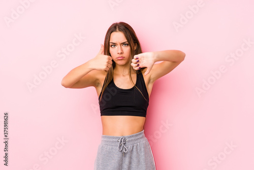 Young caucasian fitness woman posing in a pink background showing thumbs up and thumbs down, difficult choose concept © Asier