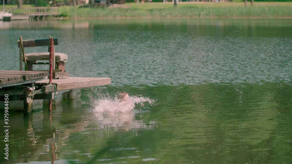 Young boy with swimwear jumps into the water from the wooden pier.