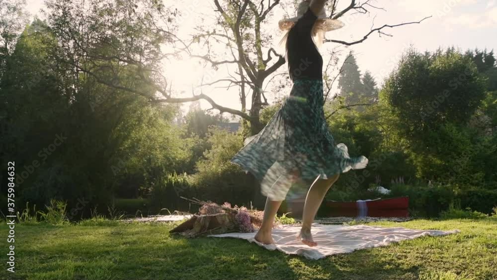 Young woman swirling around in park during picnic with sun shining through trees, dress is swaying around in air, hipster girl with straw hat, slow motion Young woman swirling around in park during picnic with sun shining through trees, dress is swaying around in air, hipster girl with straw hat, slow motion