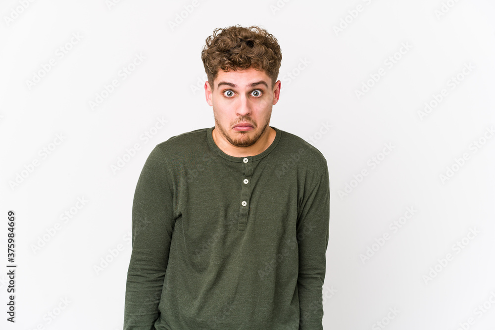 Young blond curly hair caucasian man isolated shrugs shoulders and open eyes confused. Young blond curly hair caucasian man isolated shrugs shoulders and open eyes confused.