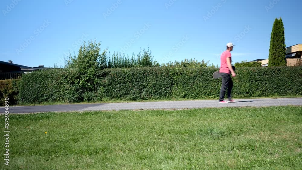 Young man walking up a hill with his skateboard in hand Young man walking up a hill with his skateboard in hand