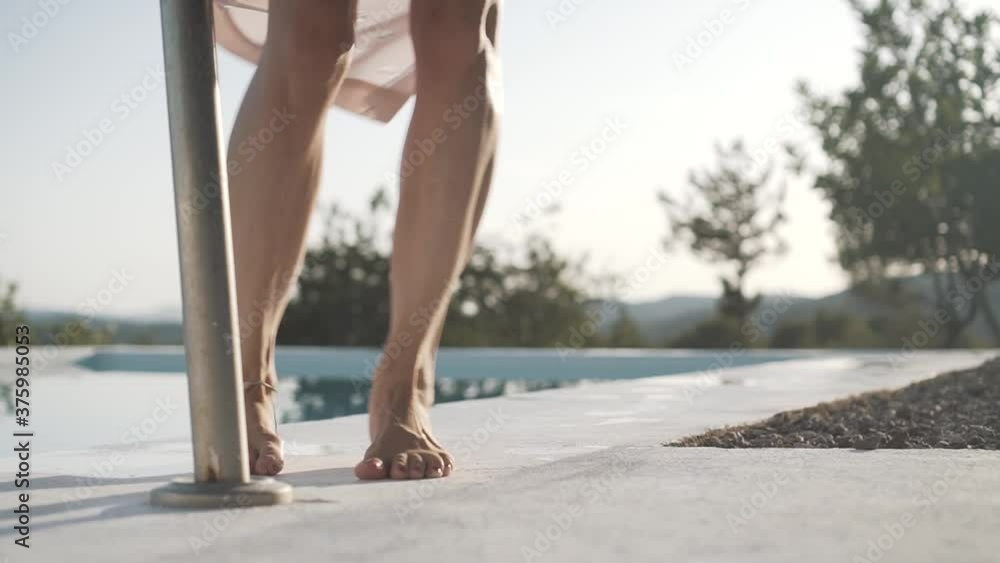 Young woman with long dress and straw hat dancing barefoot and doing a spin alongside a pool on a mountain in Ibiza, Spain at sunset. Shot in slow motion.